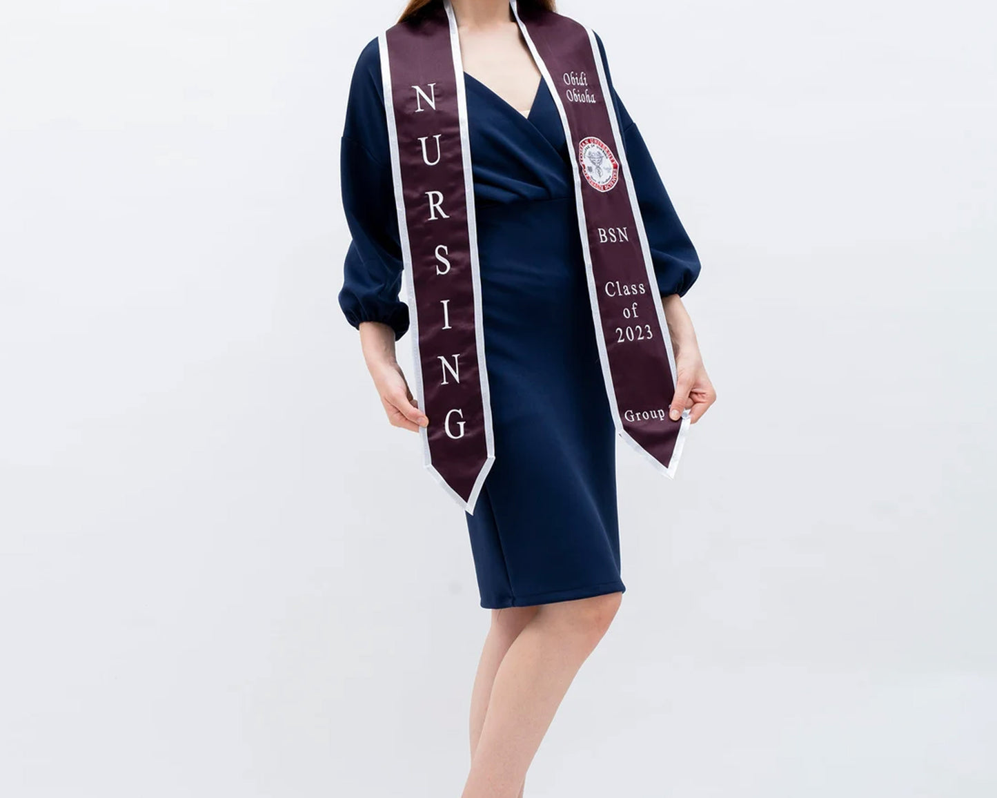 A woman in a stylish navy dress showcases a maroon and white BSN graduation sash with embroidered lettering, celebrating the Class of 2023.