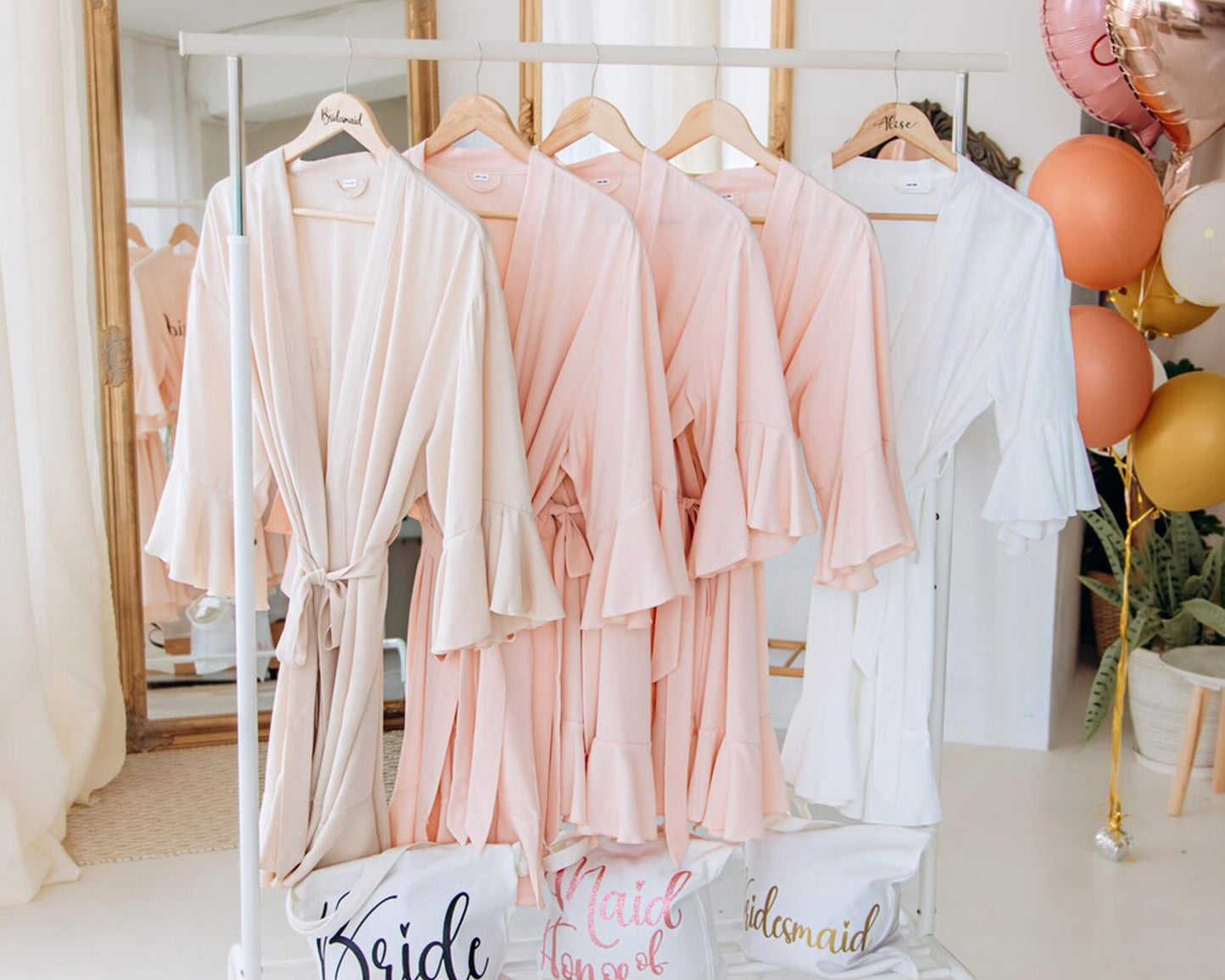 A collection of robes on a clothing rack, personalized for bridesmaids and the bride, with elegant script embroidery.
