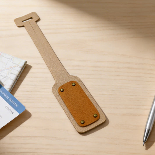 Brown leather luggage tag on a wooden surface with a pen and book in the background