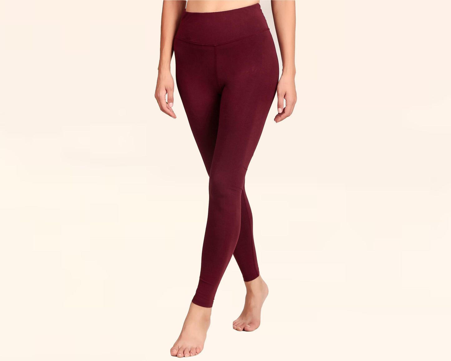 Woman wearing high-waisted burgundy leggings, walking barefoot against a neutral background.