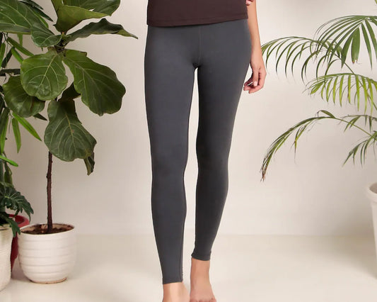 Woman wearing grey leggings in a minimal indoor setting with green plants.