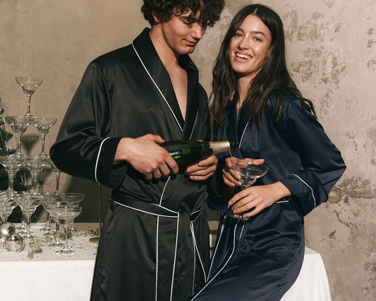 A man and woman in satin robes share a moment while pouring champagne.