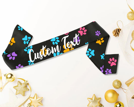 Black sash with colorful paw prints and "Custom Text" written in white, surrounded by gold and festive decorations.