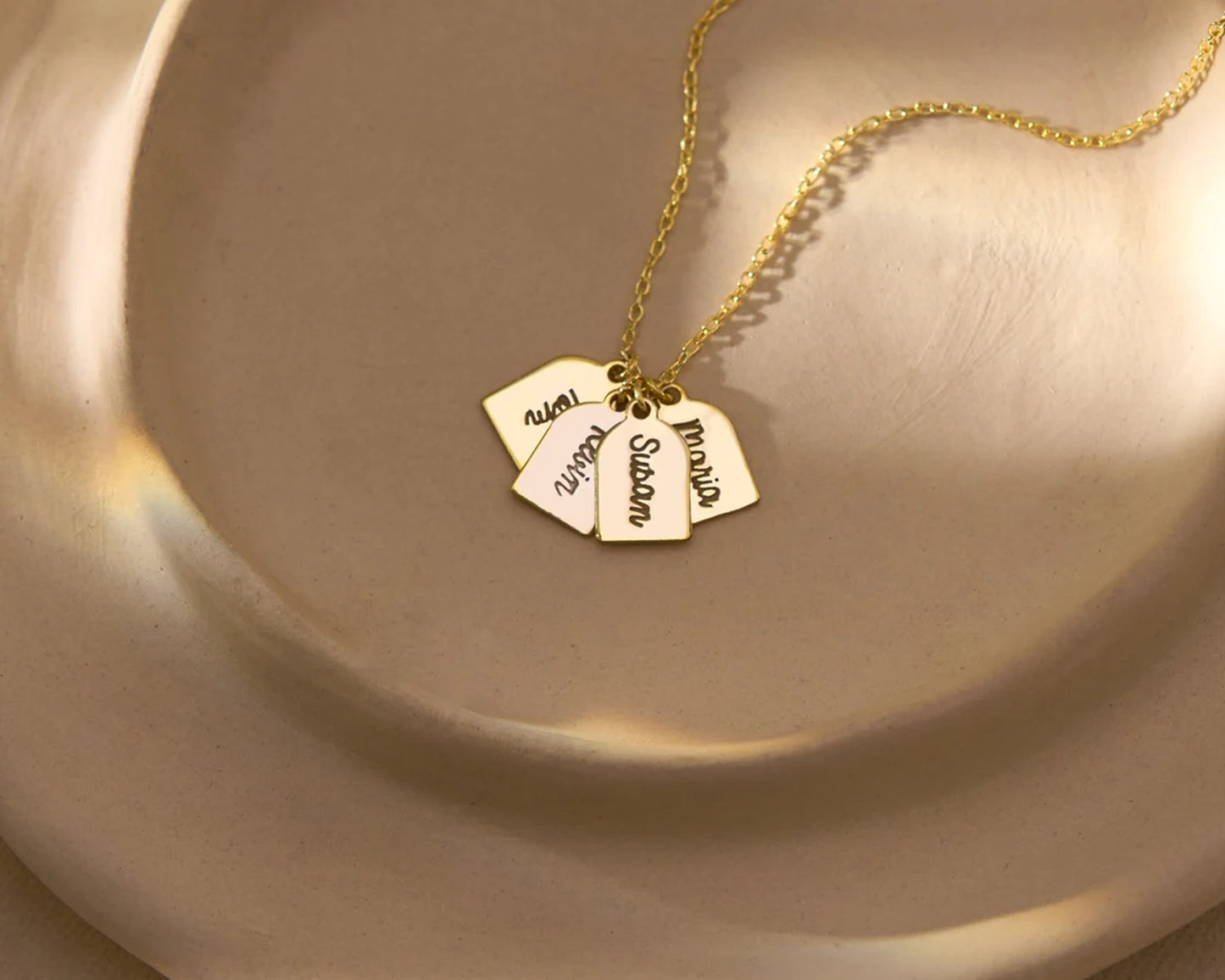 Elegant gold necklace with multiple engraved name tags displayed on a neutral plate.