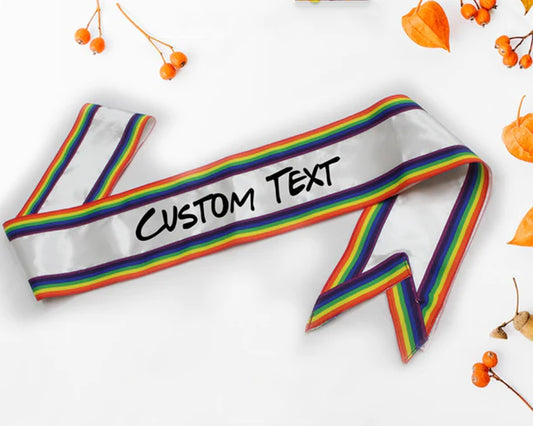 A white sash with rainbow borders featuring customizable text, displayed with orange berries on a white background.