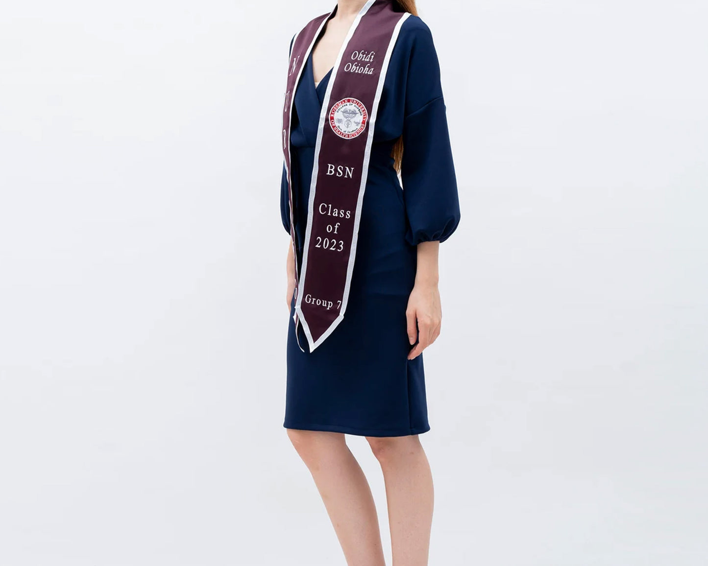 A woman in a navy dress wears a maroon and white nursing graduation stole, embroidered with her name and Class of 2023 details.