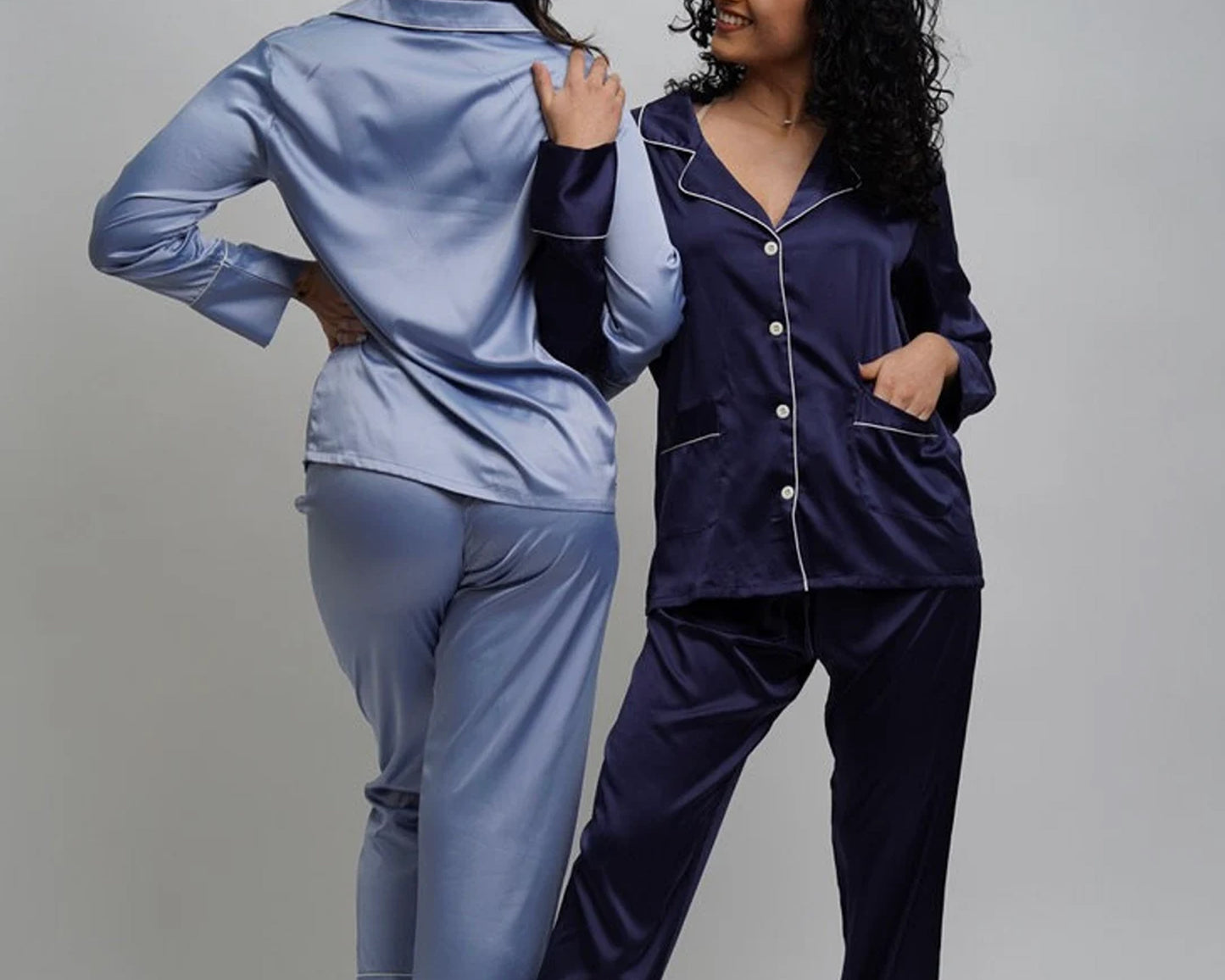 A woman wearing a blush pink satin pajama featuring button-up tops with contrast piping and matching pants