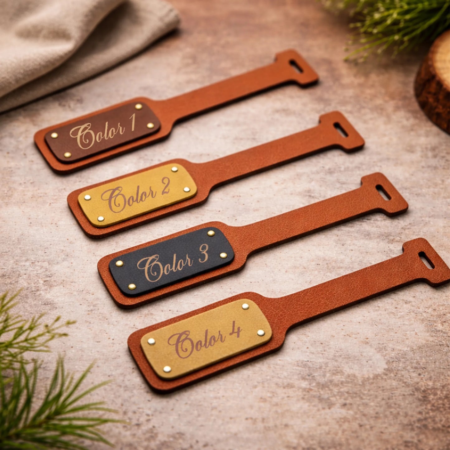 Four leather name tags in different colors on a textured surface with greenery.