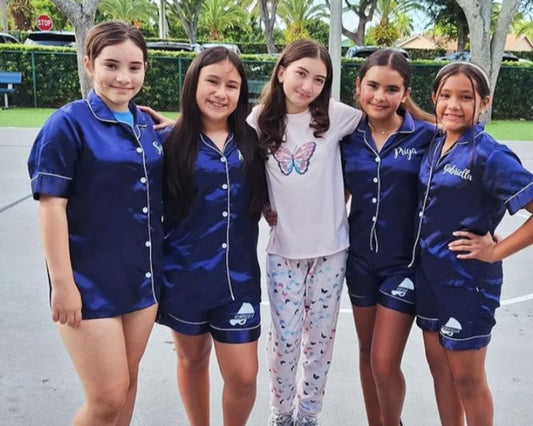 Girls in matching navy blue satin pajamas posing outdoors.