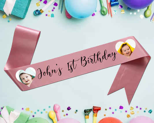 Pink ribbon with "John's 1st Birthday" and two baby photos in heart-shaped cutouts.