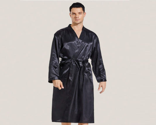 A male model wearing a sleek black satin robe with a tie belt, long sleeves, and a smooth, luxurious finish.