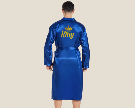 A male model wearing a royal blue satin robe with "King" and a gold crown embroidered on the back. The robe has a smooth, silky finish and a matching tie belt.
