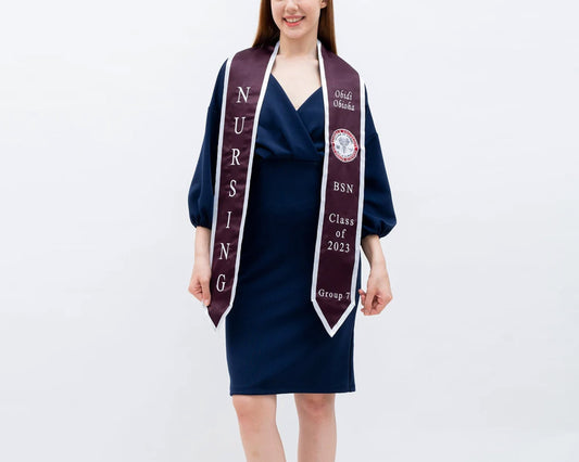 A woman in a navy blue dress wears a maroon and white nursing graduation stole with embroidered text for the BSN Class of 2023.