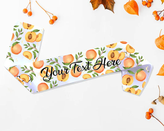 A satin sash with a vibrant peach pattern and customizable text, displayed on a white background with autumn leaves and berries.