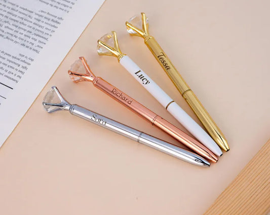 A set of four elegant pens with diamond-shaped tops, personalized with names, in gold, silver, rose gold, and white finishes.