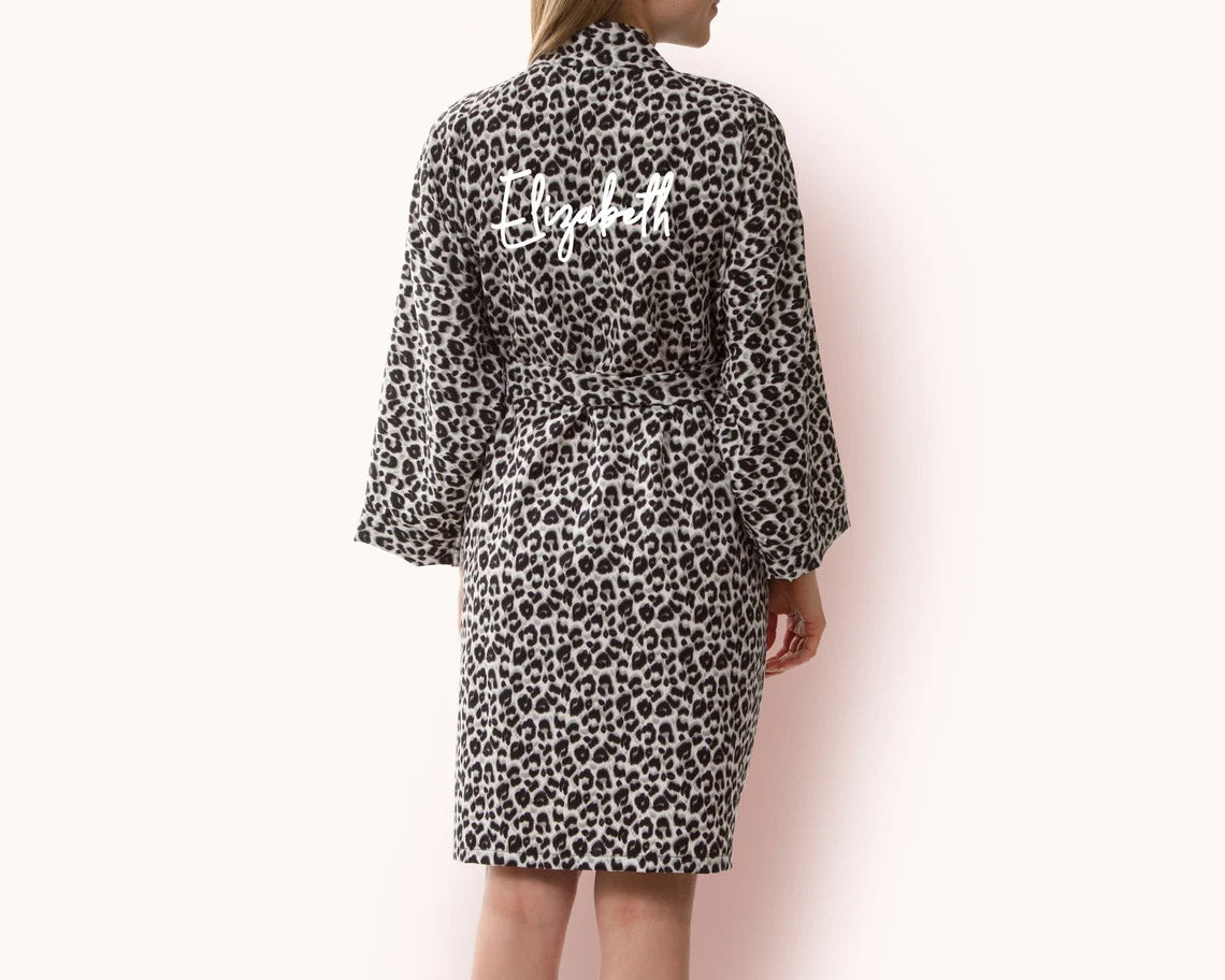 Woman wearing a leopard print fleece robe with a waist tie, featuring personalized white script text "Elizabeth" on the back.