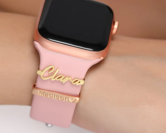 Close-up of a pink Apple Watch band featuring two personalized name charms in gold, engraved with "Clara" and "Madison♥".