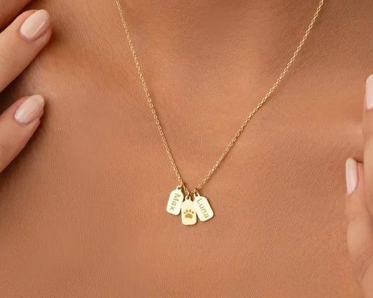 Gold necklace with engraved pet name tags featuring a paw print charm.