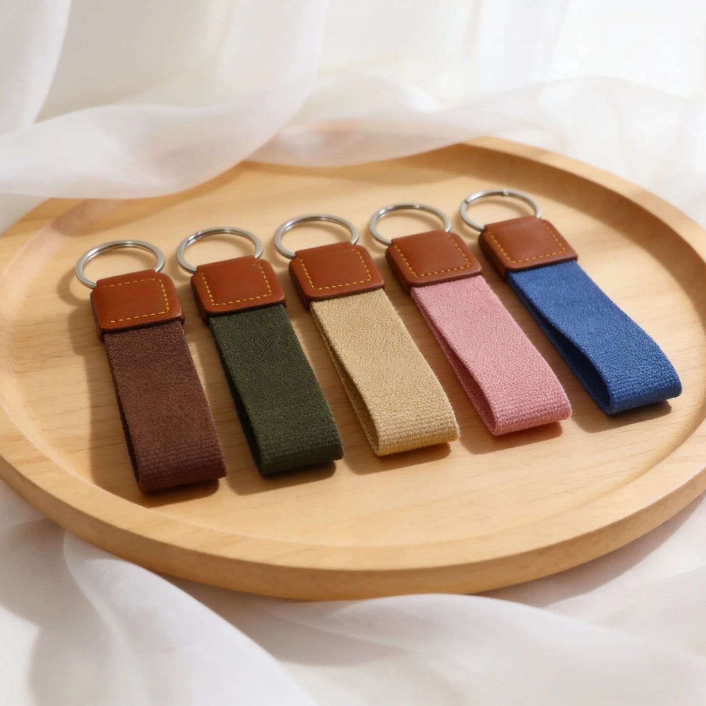 Set of five keychains with brown leather ends on a wooden tray