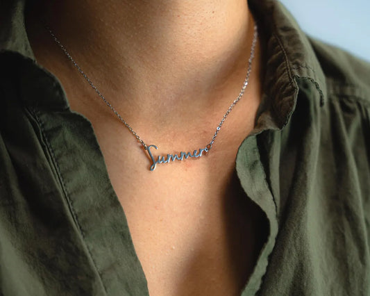 Close-up of a silver custom name necklace spelling "Summer," worn with a dark green shirt.