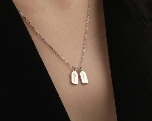 Elegant silver necklace with two engraved name tags, "Emma" and "Jacob," worn over a black outfit.