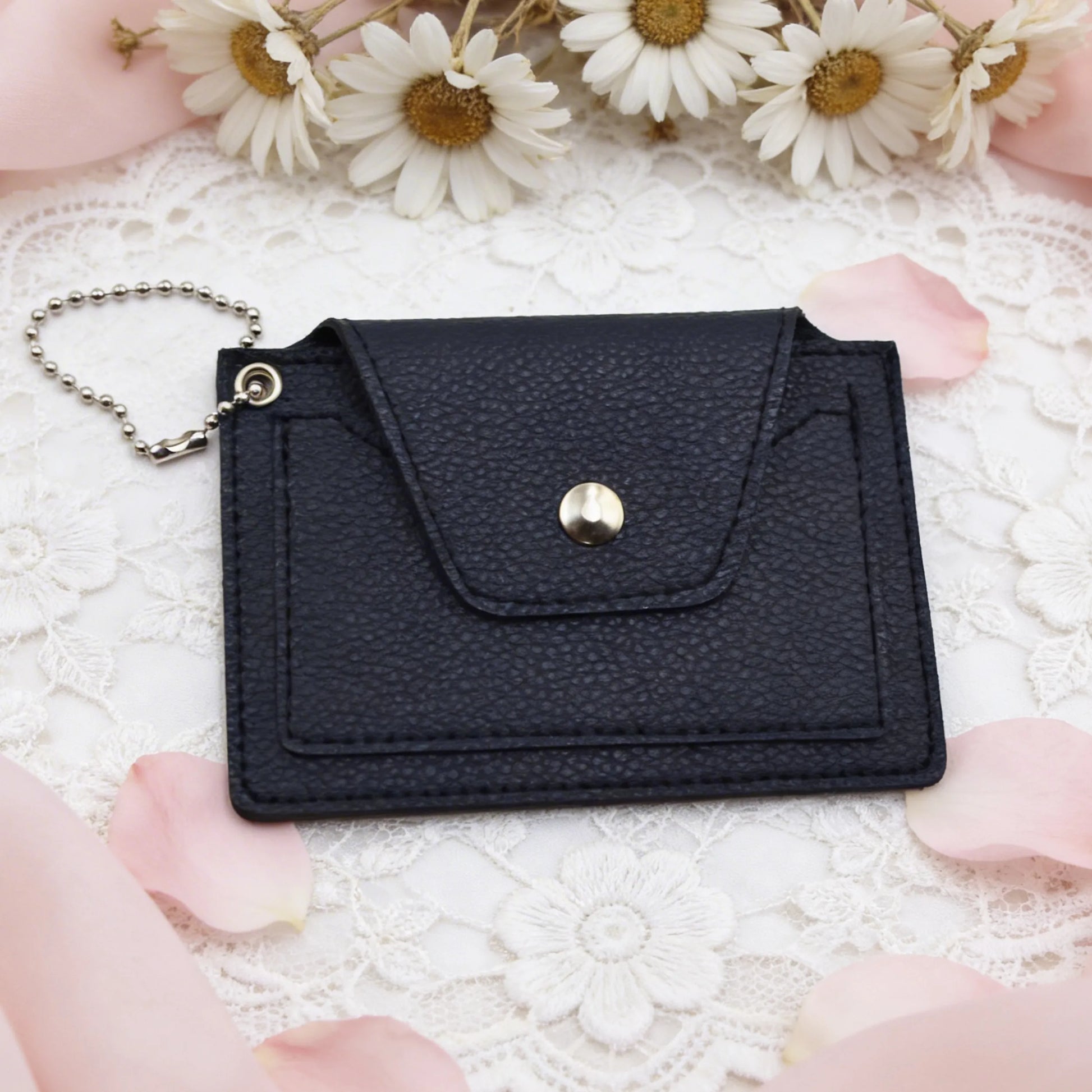 Black leather wallet with a gold button on a white lace background with flowers