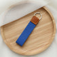 Blue keychain with brown leather tag on a wooden tray