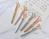 Stylish diamond-topped pens in gold, pink, white, silver, and rose gold, engraved with "Bride," "Maid of Honor," and "Bridesmaid," arranged on handwritten paper.