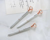Elegant silver and white diamond-topped pens with rose gold accents, engraved with "Bridesmaid" and "Bride," placed on a white surface with handwritten notes.
