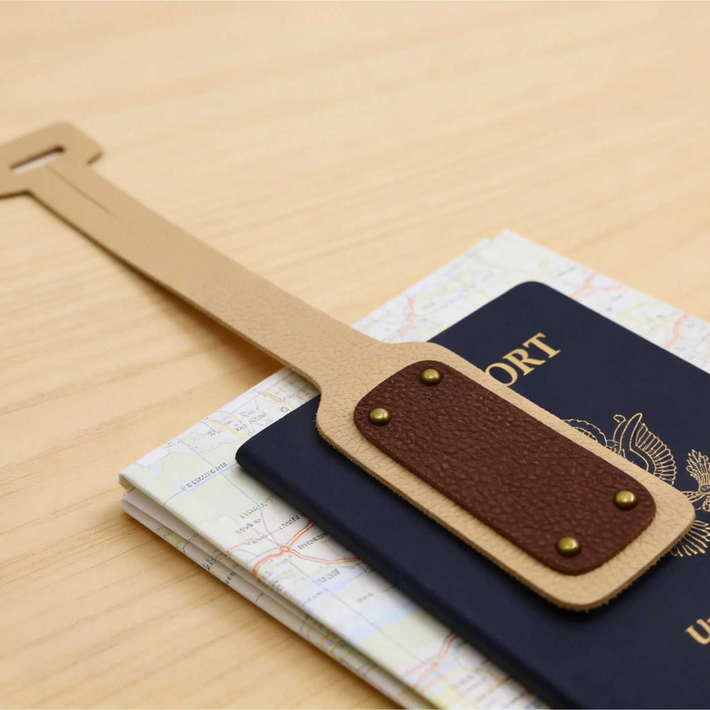 Brown leather luggage tag on top of a passport and map on a wooden surface