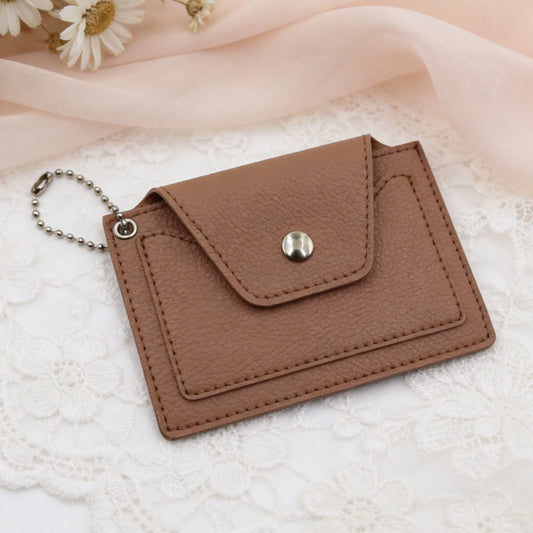 Brown leather cardholder with a keychain on a textured surface with flowers in the background