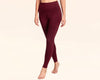 Woman wearing high-waisted burgundy leggings, walking barefoot against a neutral background.