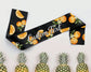 A black satin sash featuring vibrant orange slices and blossoms, customizable text, and a tropical pineapple backdrop.