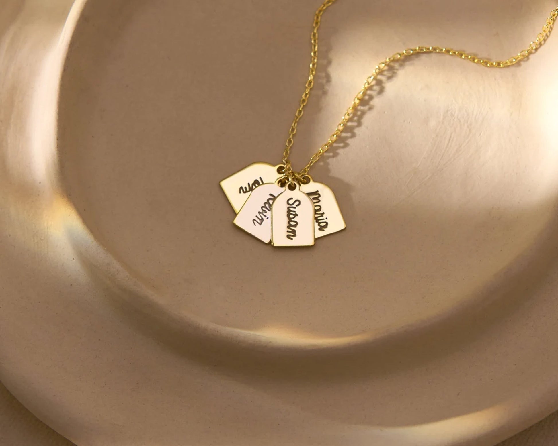 Elegant gold necklace with multiple engraved name tags displayed on a neutral plate.
