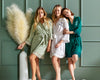 Bridal party in lace-trimmed robes, posing against a green wall.