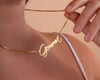  A stylish gold name necklace spelling "Gemma," held gently by a woman wearing a white top, showcasing its delicate cursive design.