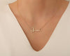 Close-up of a delicate gold custom name necklace spelling "Olivia," worn with a white V-neck top.