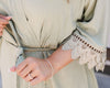 Close-up of a woman's hand adjusting the belt of a soft green robe with intricate lace sleeves.
