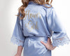 A young girl wearing a light blue satin robe with lace trim and "Flower Girl" written in gold on the back.