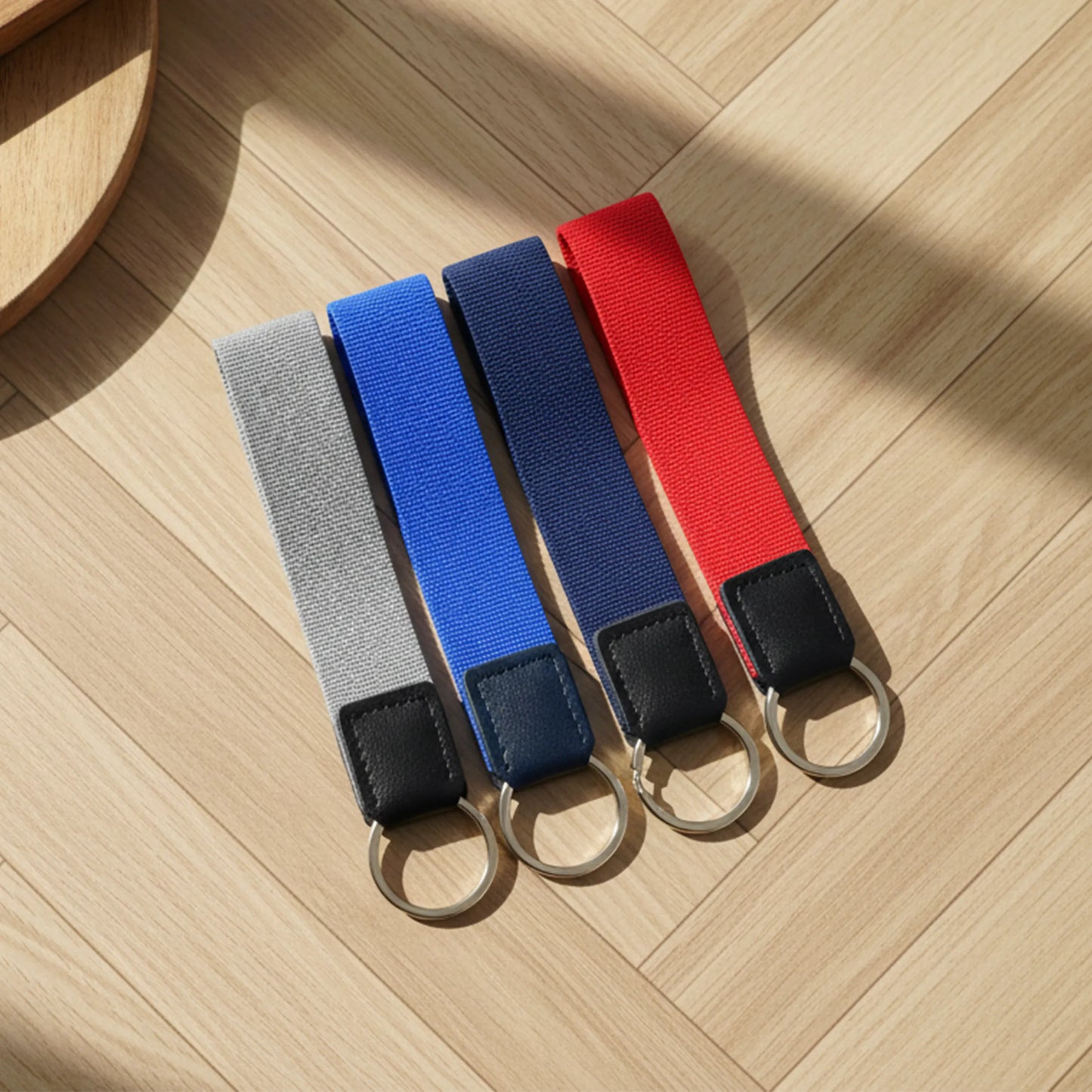 Four keychain straps in gray, blue, red, and black on a wooden surface
