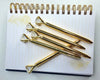 A set of gold diamond-topped pens arranged on a spiral-bound notebook with lined pages and gold peacock feather designs.