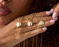  A close-up of a hand adorned with multiple gold tag necklaces, each featuring engraved names, against a warm-toned background.