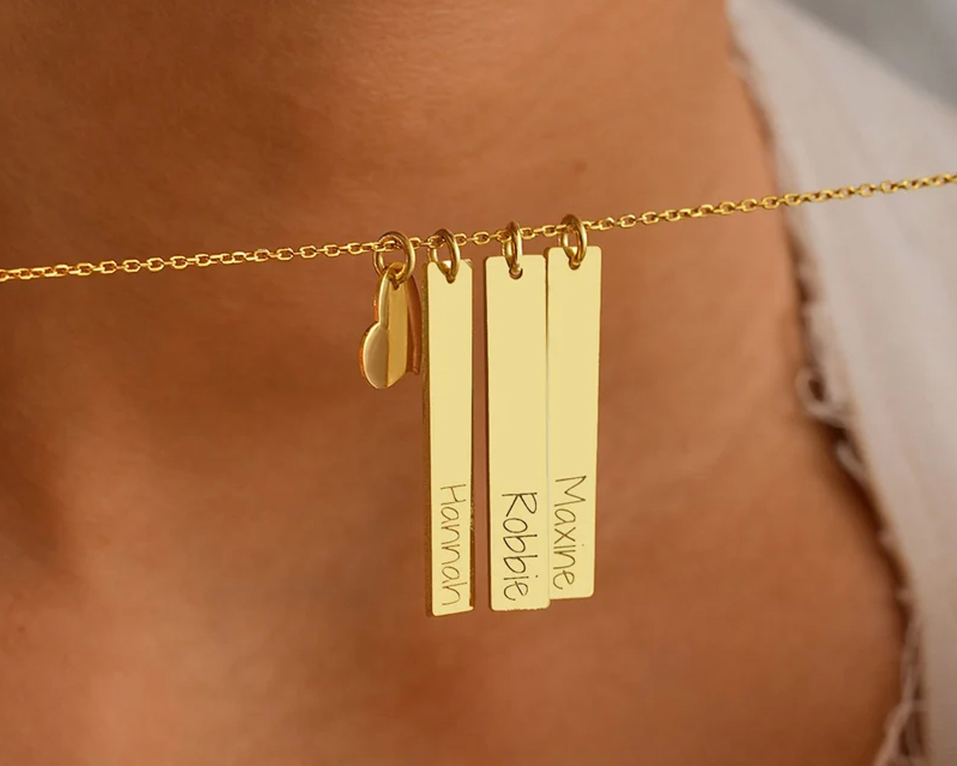 A personalized gold bar necklace with multiple engraved name pendants, elegantly displayed on a woman's neck.