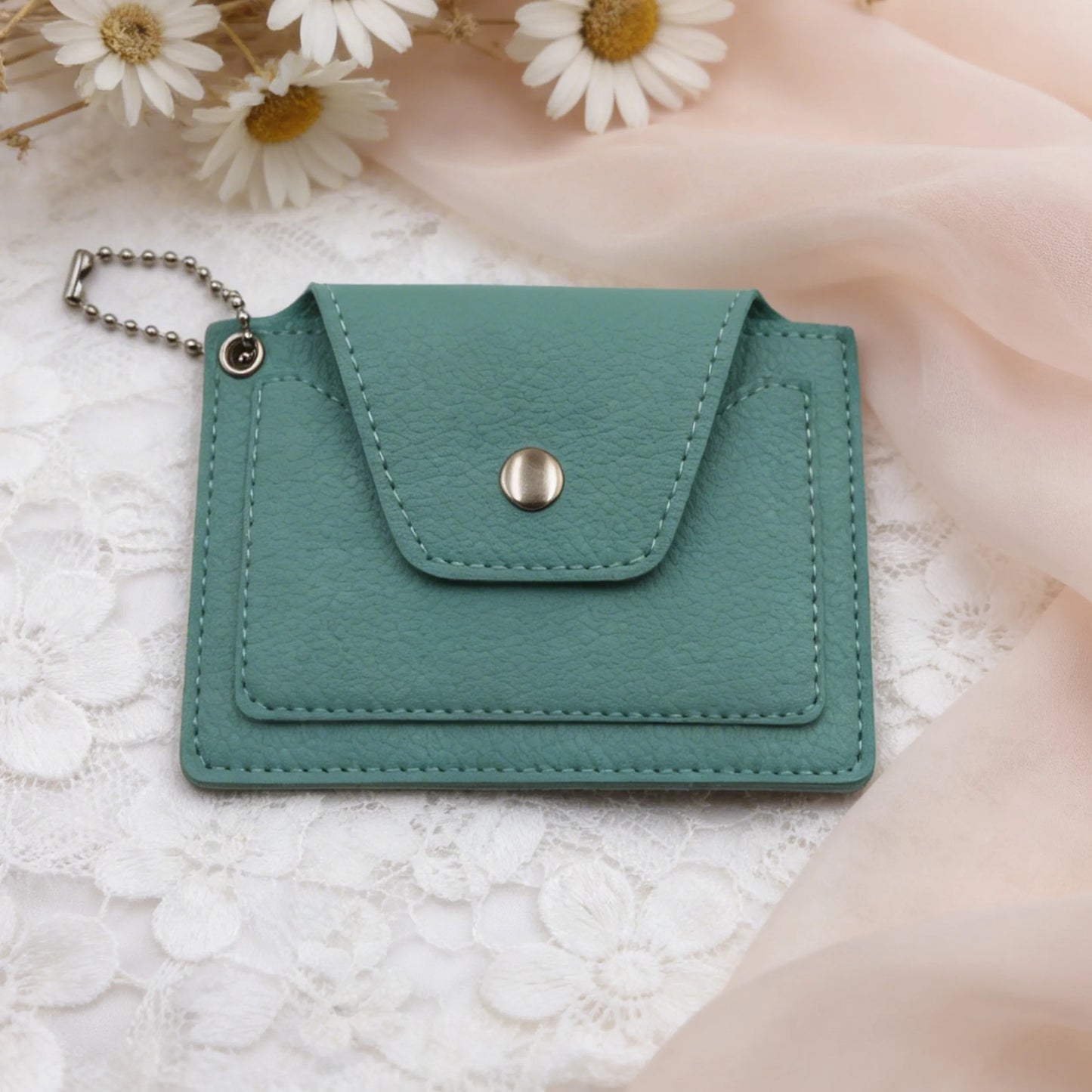 Green leather cardholder with a metal clasp on a light textured surface with flowers in the background