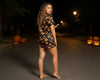 Woman in a Halloween-themed dress standing on a street at night with pumpkins around.