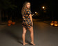 Woman in a Halloween-themed dress standing on a street at night with pumpkins around.