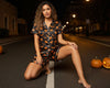 Woman in Halloween-themed pajamas sitting on a street at night with pumpkins around.
