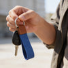 Hand holding a key with a blue strap against a blurred outdoor background