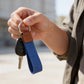 Hand holding a key with a blue strap against a blurred outdoor background