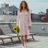 Woman walking on a terrace holding a sunflower wearing a pink gingham sleepshirt with Isla embroidered on the pocket